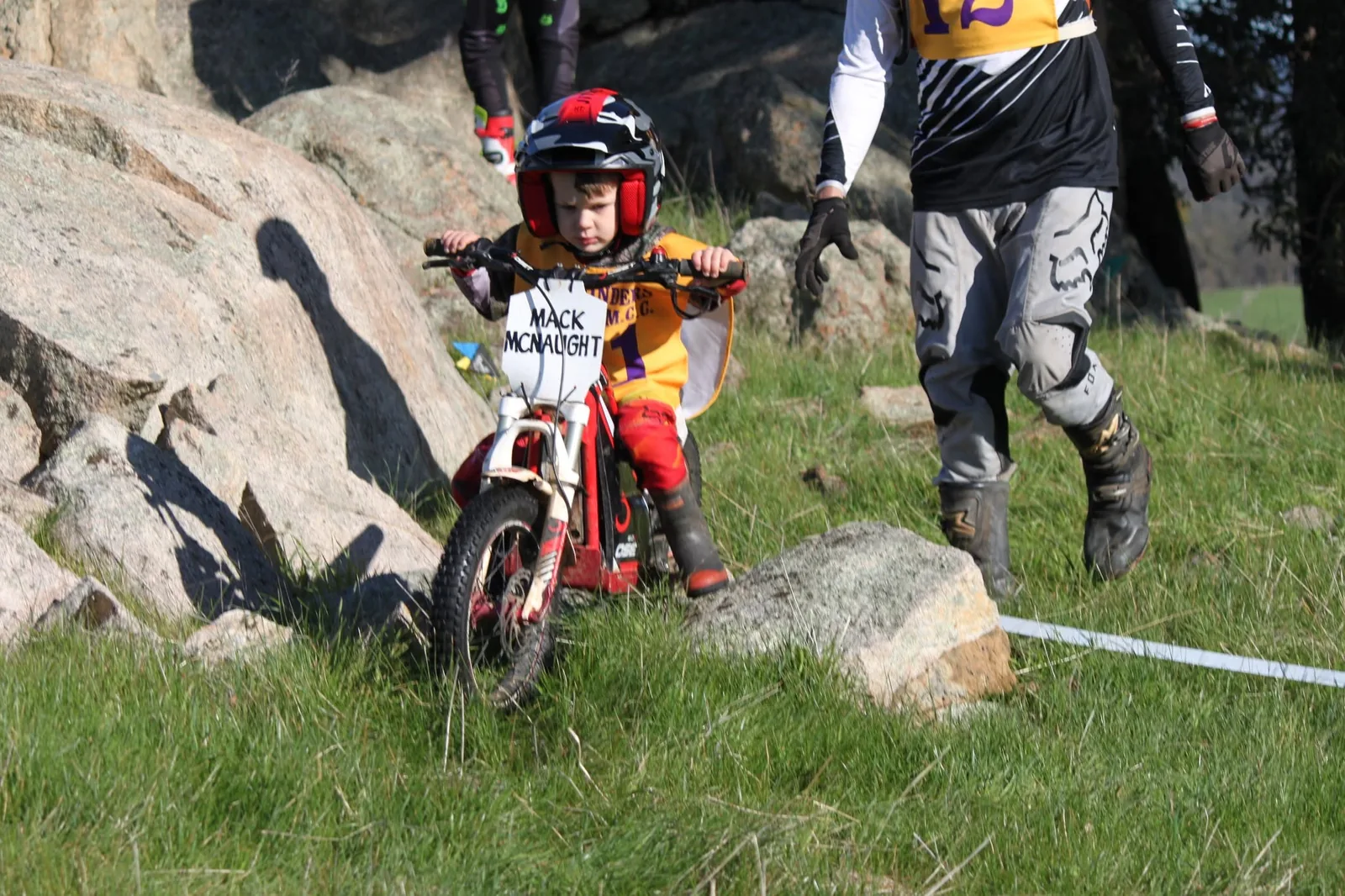 Very small junior rider negotiating a grassy section with an adult walking alongside