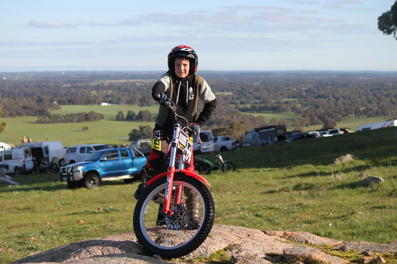 Junior rider smiling on a small trials bike with the paddock and WA landscape behind